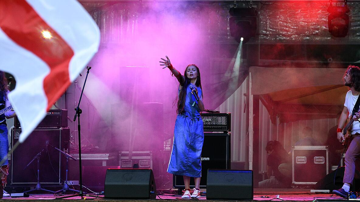 Eine Band aus drei Personen bestehend steht auf der Bühne, linker Nebel im Hintergrund, die Sängerin reckt ihre Hand nach oben, ihre Augen sind geschlossen