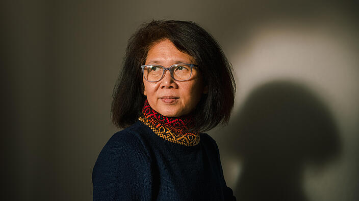 Ein Porträt von Ma Thieda mit etwa 55 Jahren. Ihre Haare sind kinnlang, sie trägt einen dunklen Pullover und eine Brille und blickt rechts an der Kamera vorbei.