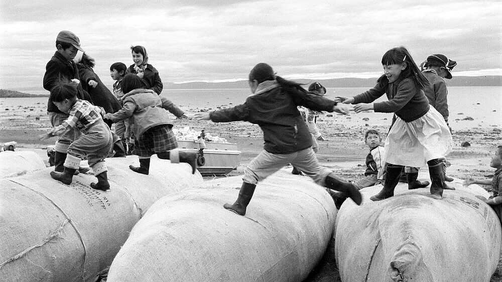 Several children jump on upturned canoes along the coast.