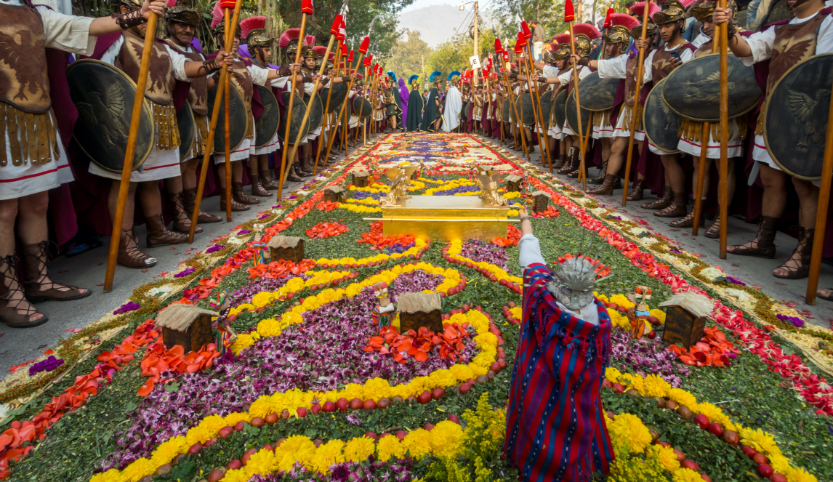 At the edge of a large, colorful carpet of flowers stand men in historical garb with spears and shields.  