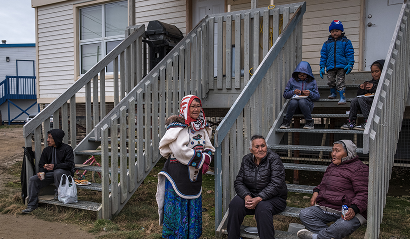 Einwohner von Cape Dorset sitzen vor ihren Häusern. Viele von ihnen leben in Sozialbauwohnungen